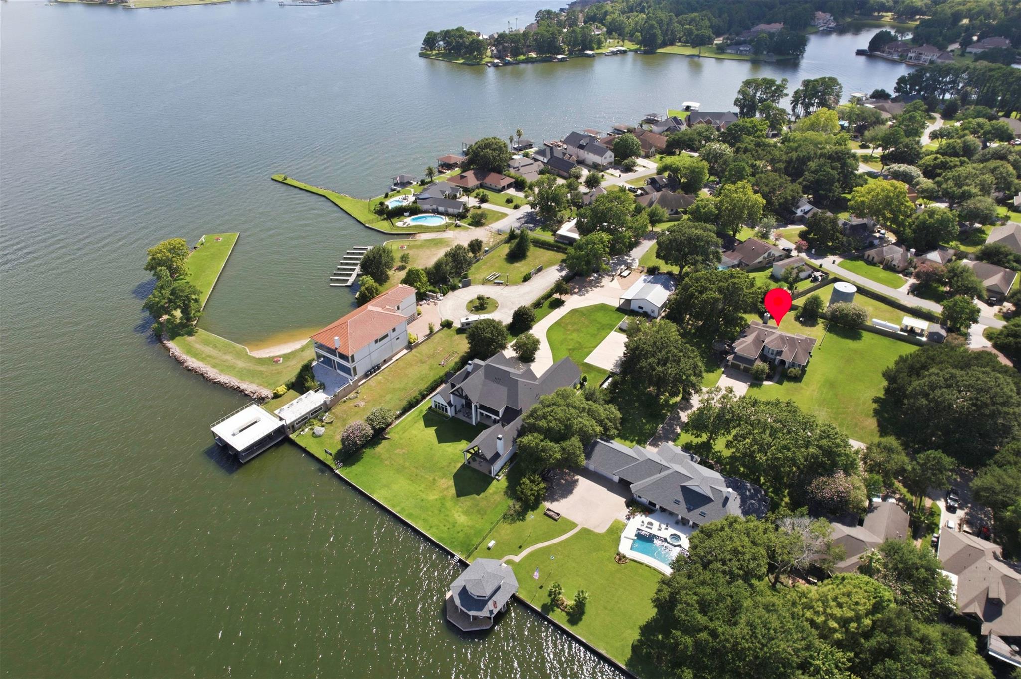 Aerial view of a marked home in a leafy lakeside neighborhood with docks and pools.