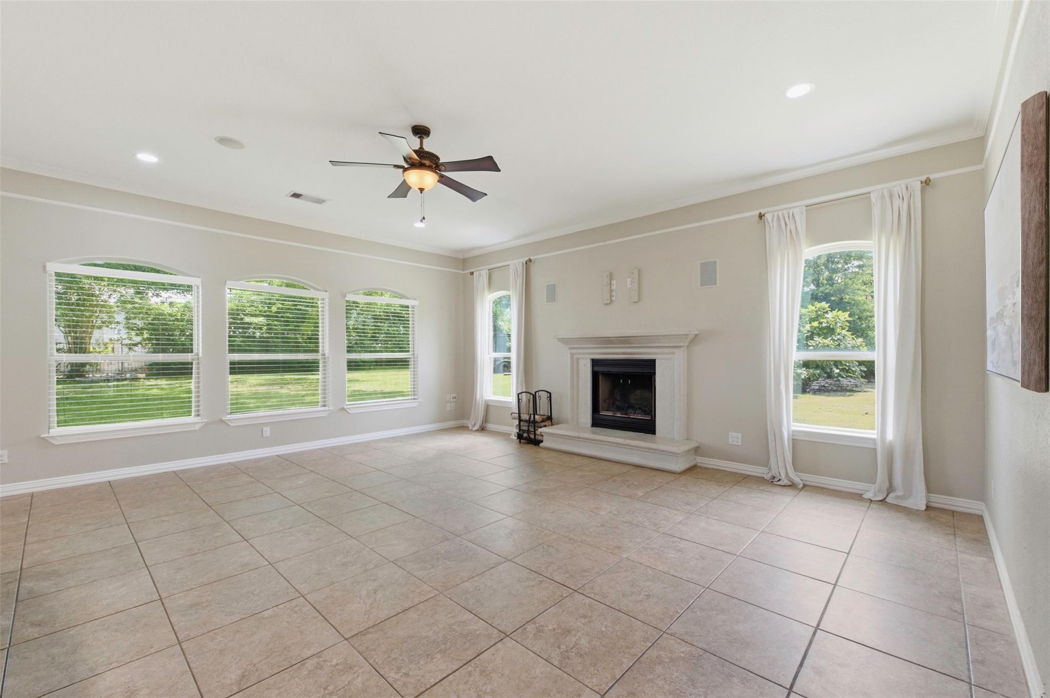 Vacant living room with tiled floors, a fireplace, and large windows overlooking a lawn.
