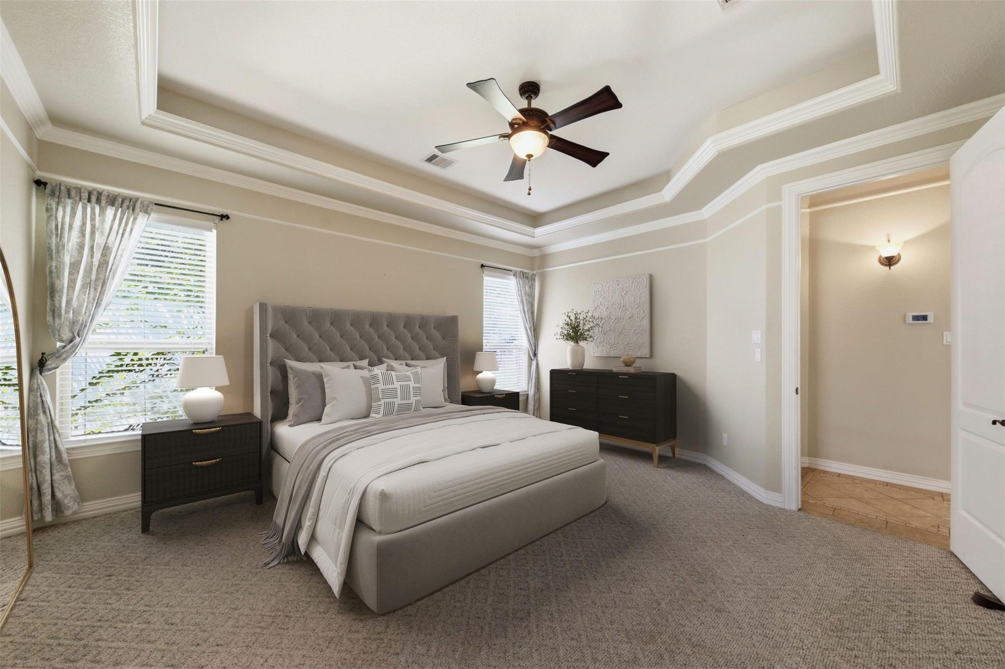 Bedroom with an upholstered bed beneath a tiered tray ceiling and ceiling fan.