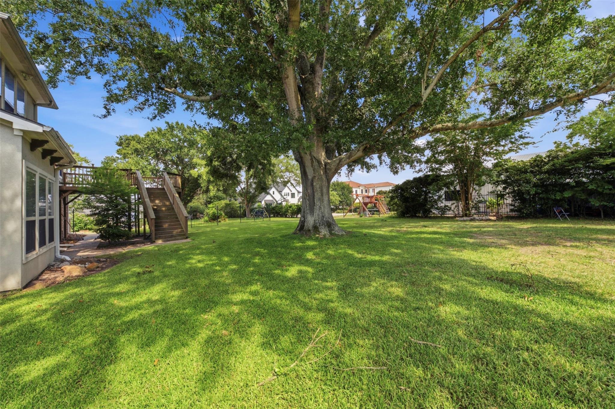 Spacious backyard with a large shade tree, grassy lawn, and raised wooden deck.