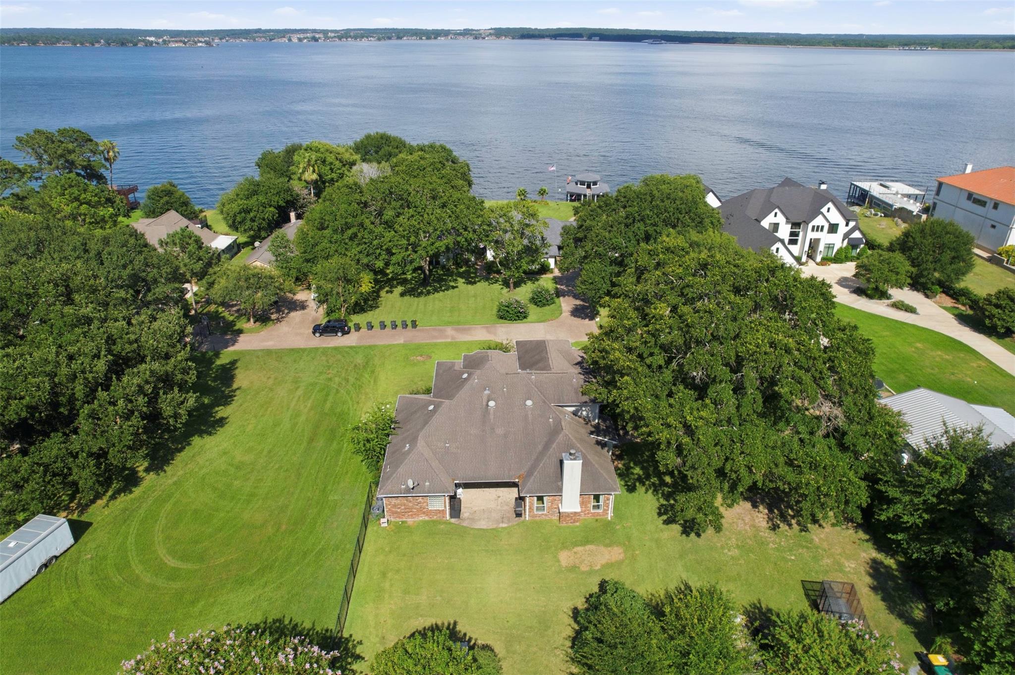 Aerial view of a lakeside home with a broad lawn and mature trees beside the lake.