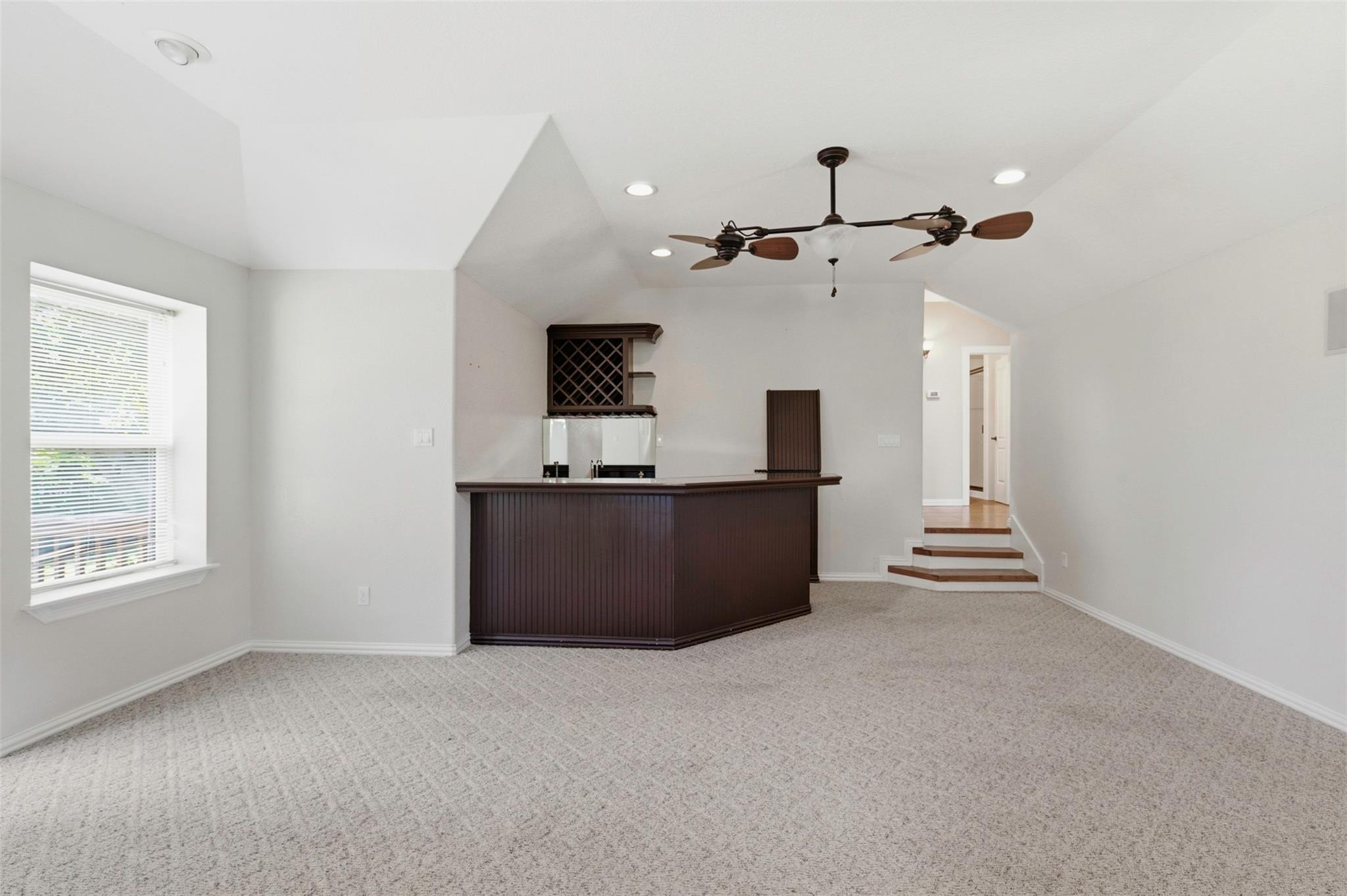 Empty carpeted room with a dark built-in wet bar, wine rack, and vaulted ceiling.