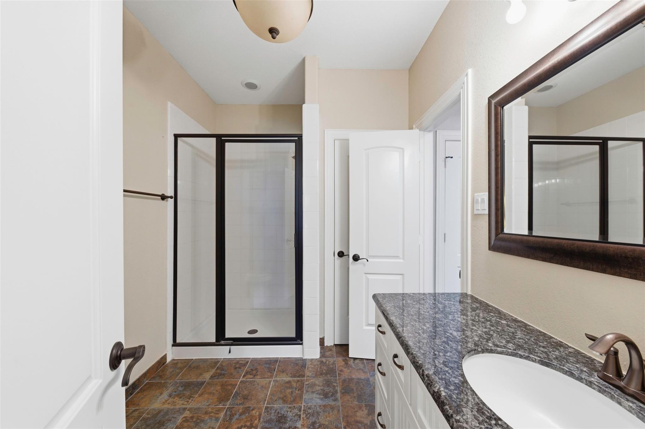 Bathroom with a black-framed glass shower and granite vanity countertop.