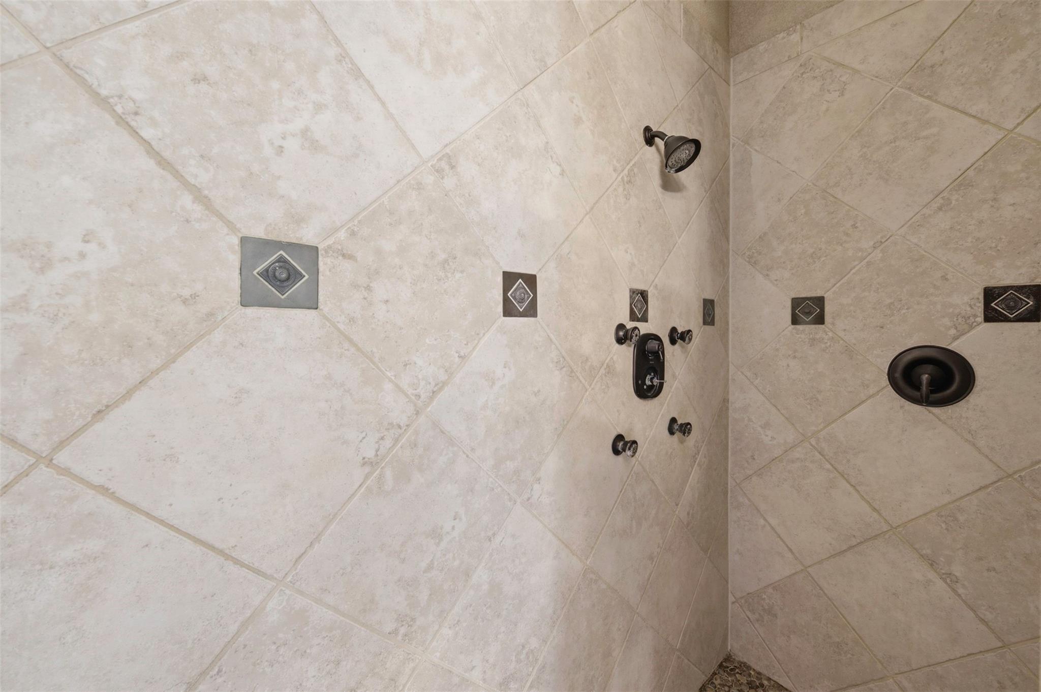Tiled shower with dark fixtures, multiple controls, and decorative diamond accents.