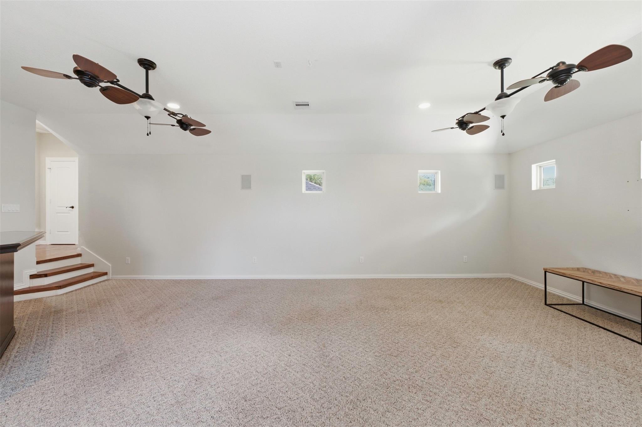 Spacious carpeted room with multiple ceiling fans, small high windows, and steps to a doorway.