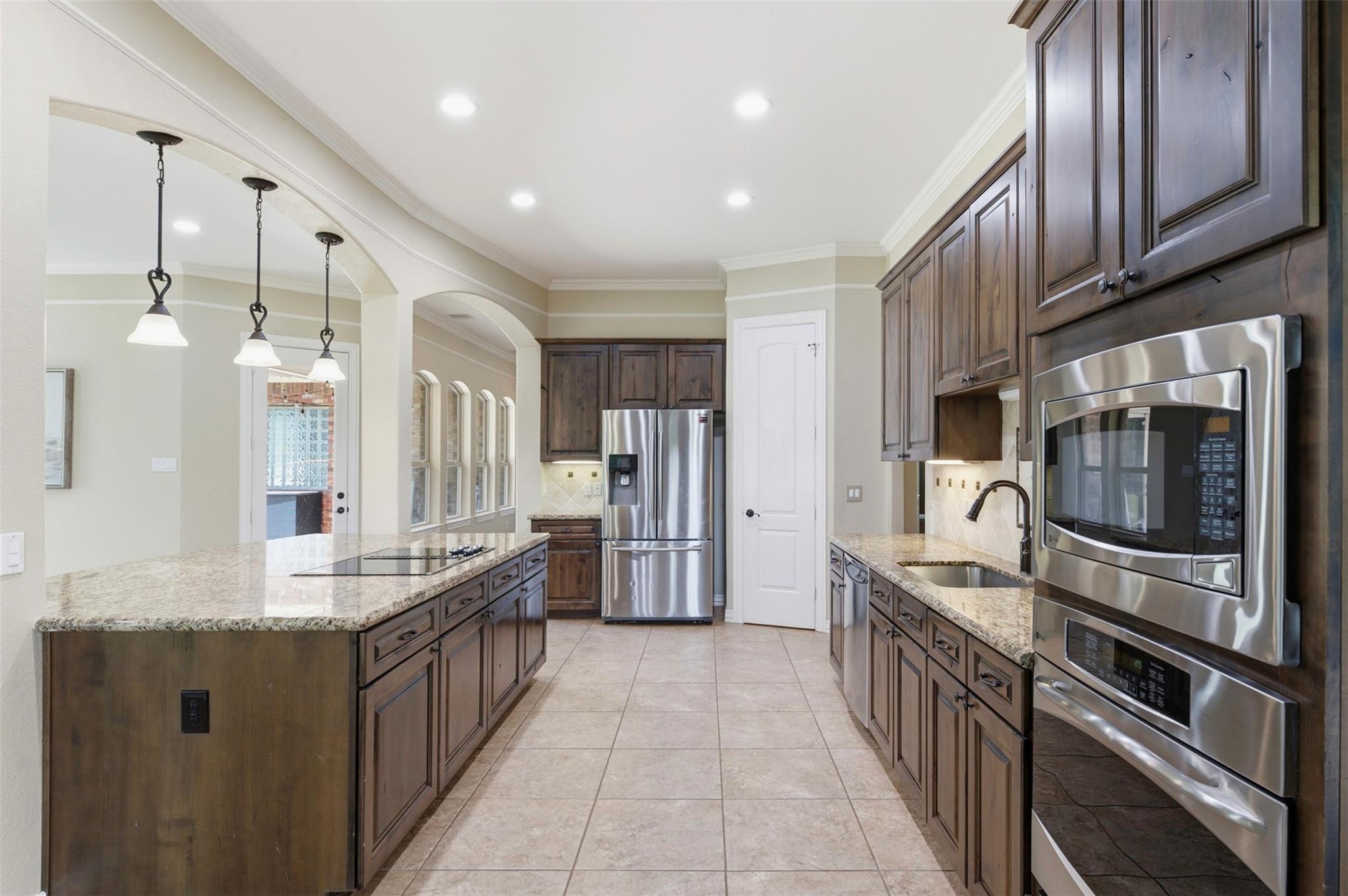 Kitchen with dark wood cabinets, granite countertops, a cooktop island, and stainless steel appliances.