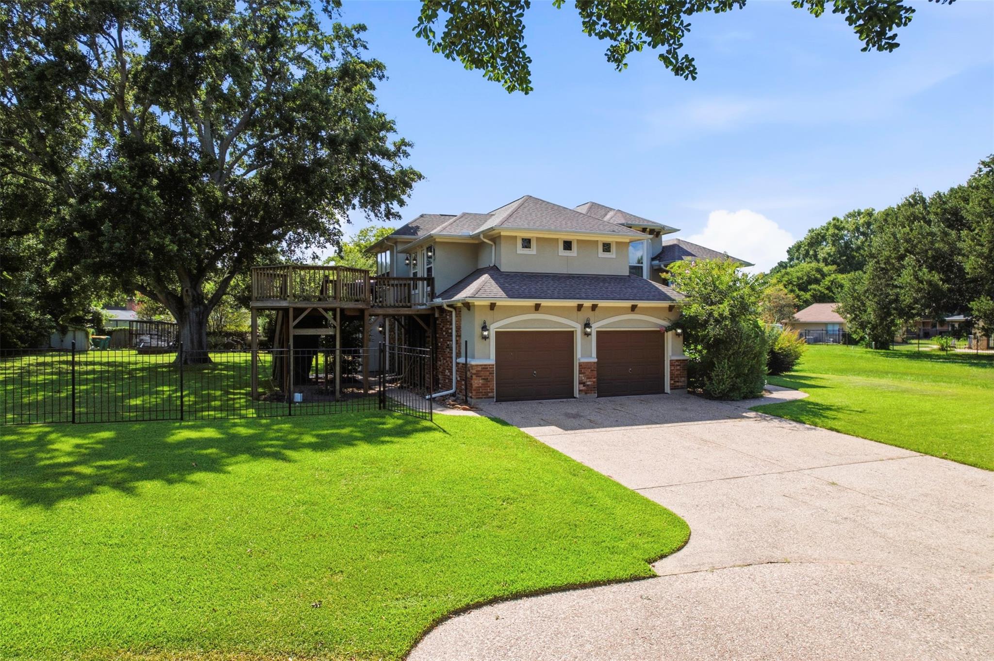 Home with a raised wooden deck, two-car garage, and broad lawn beneath mature trees.