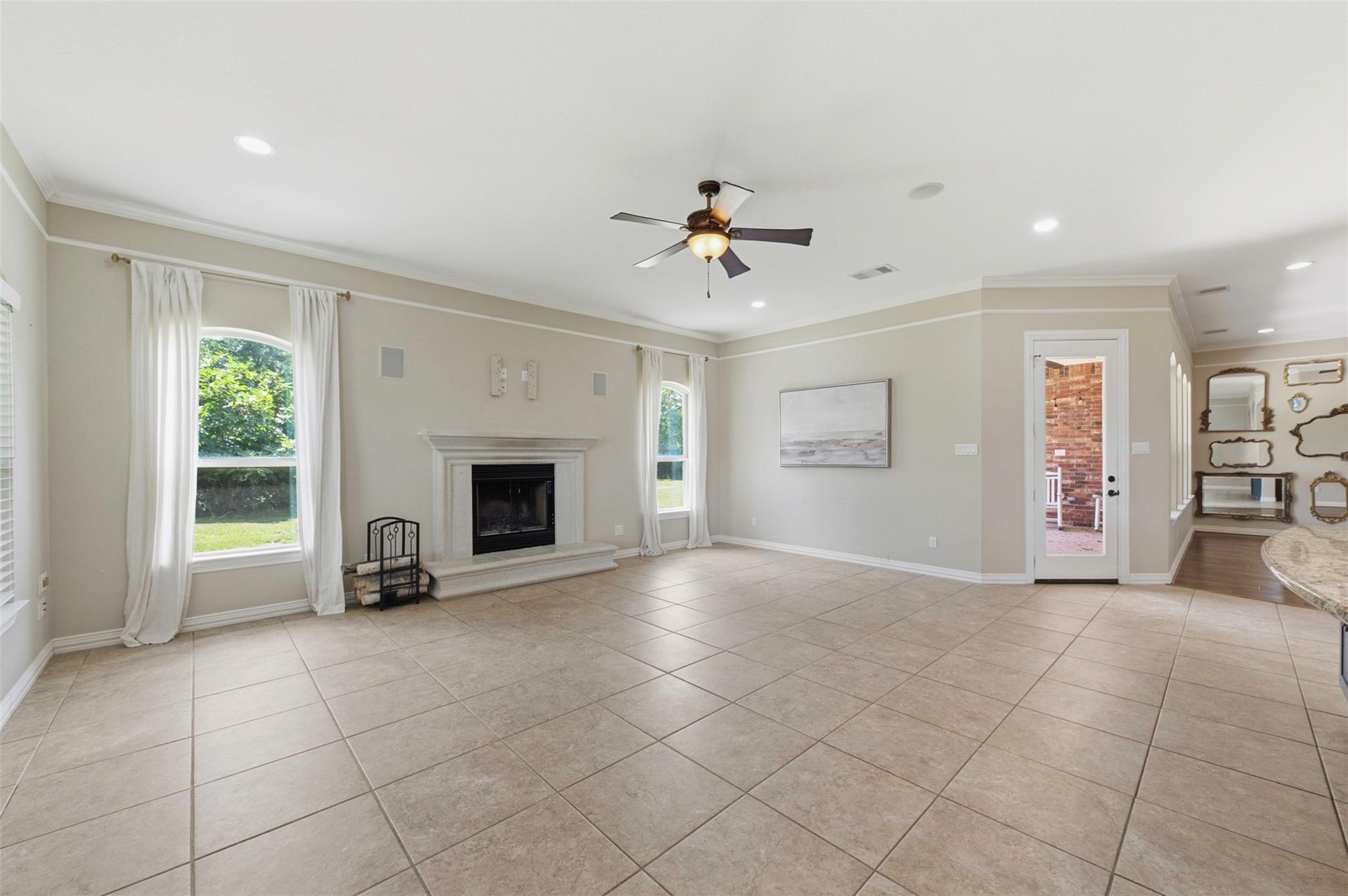 Mostly empty living room with a tiled floor, white fireplace, curtained windows, and glass patio door.
