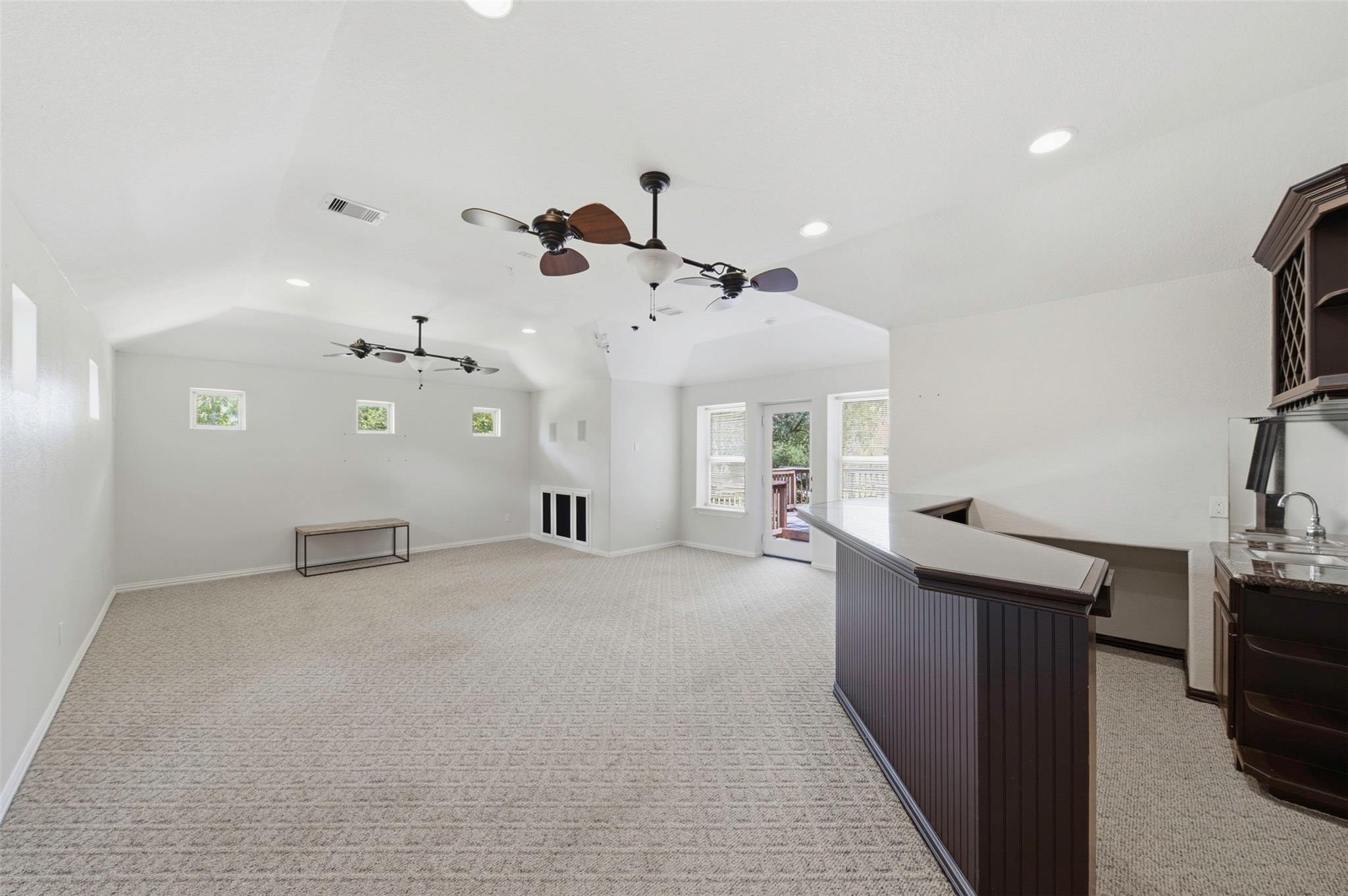 Spacious carpeted bonus room with two ceiling fans, a built-in bar, and French doors to a deck.