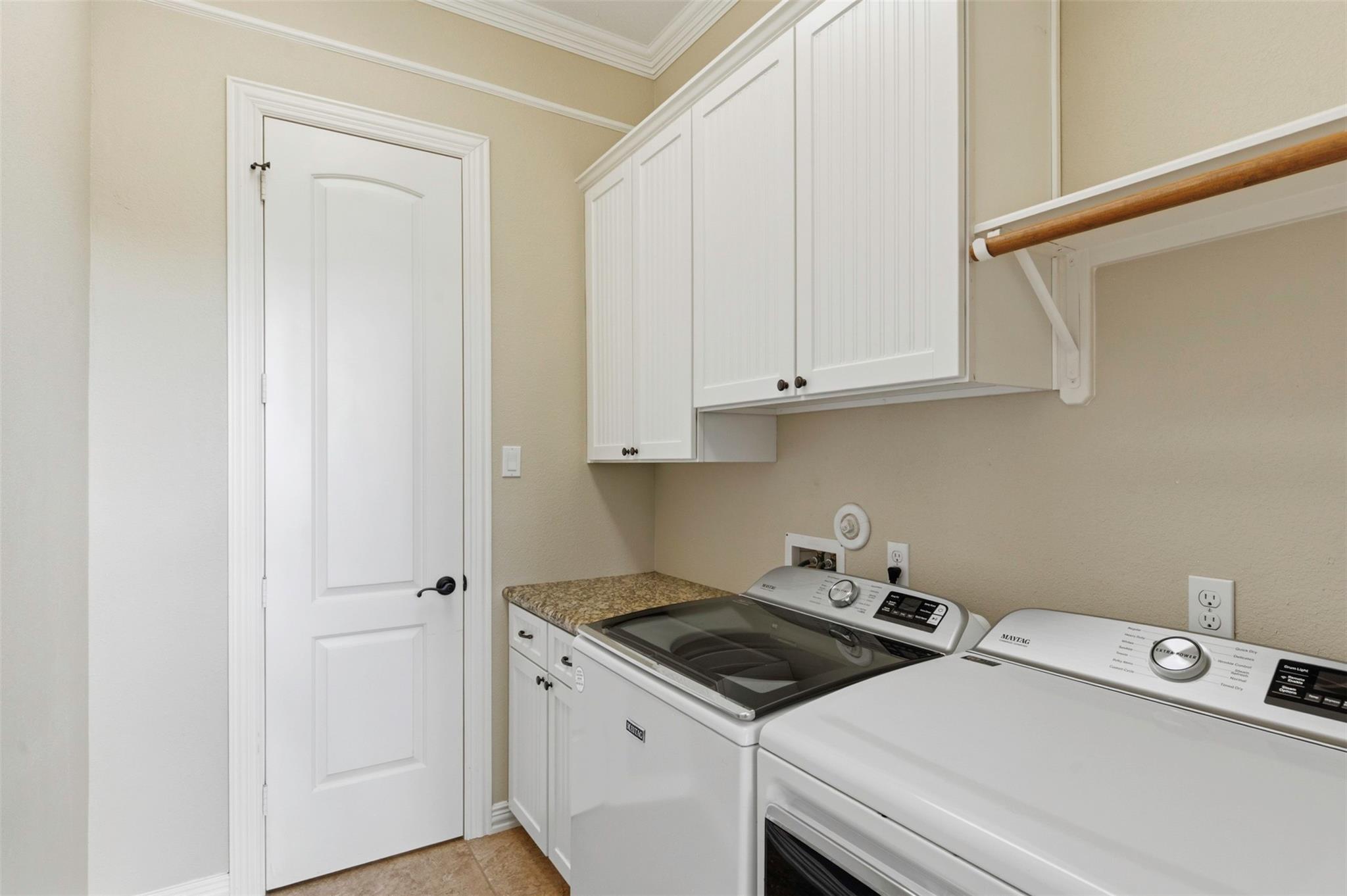 Laundry room with white washer and dryer, upper cabinets, and a wooden hanging rod.