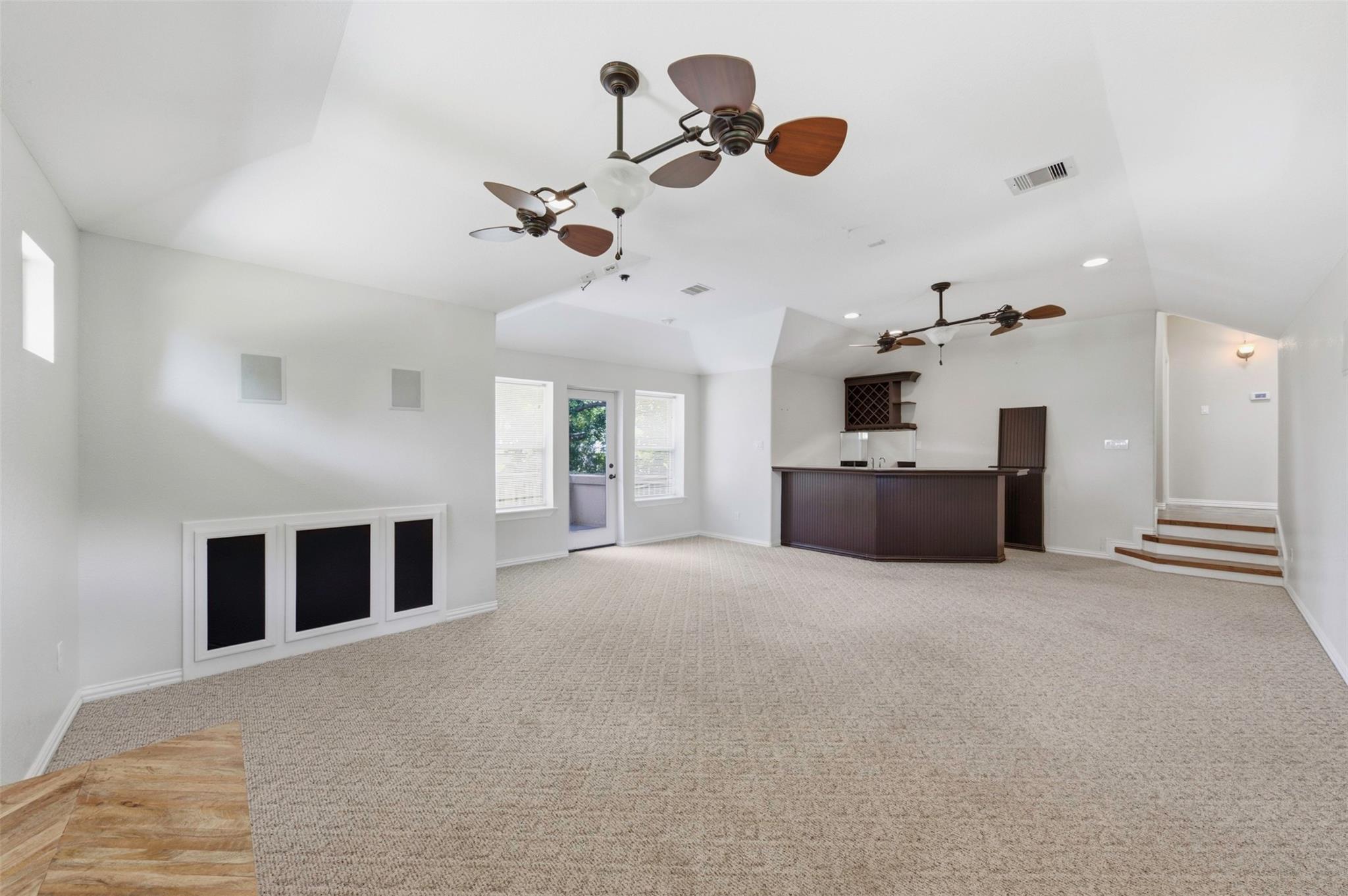 Carpeted room with a built-in bar, vaulted ceiling, ceiling fans, and steps to a hallway.