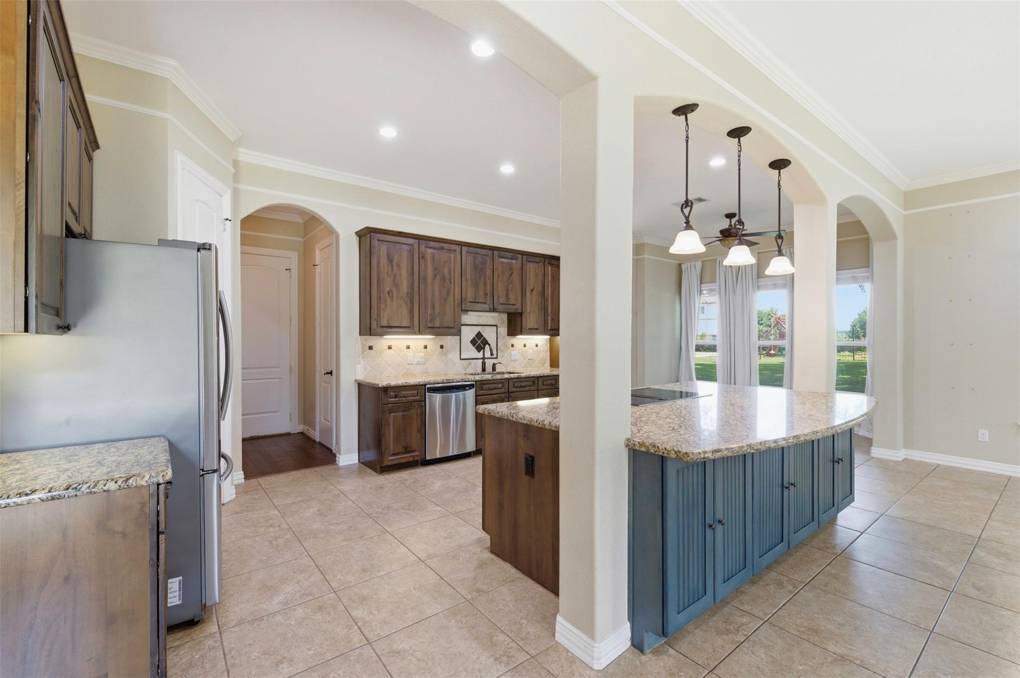 Kitchen with a blue granite-topped island, dark wood cabinetry, and arched openings to the dining area.