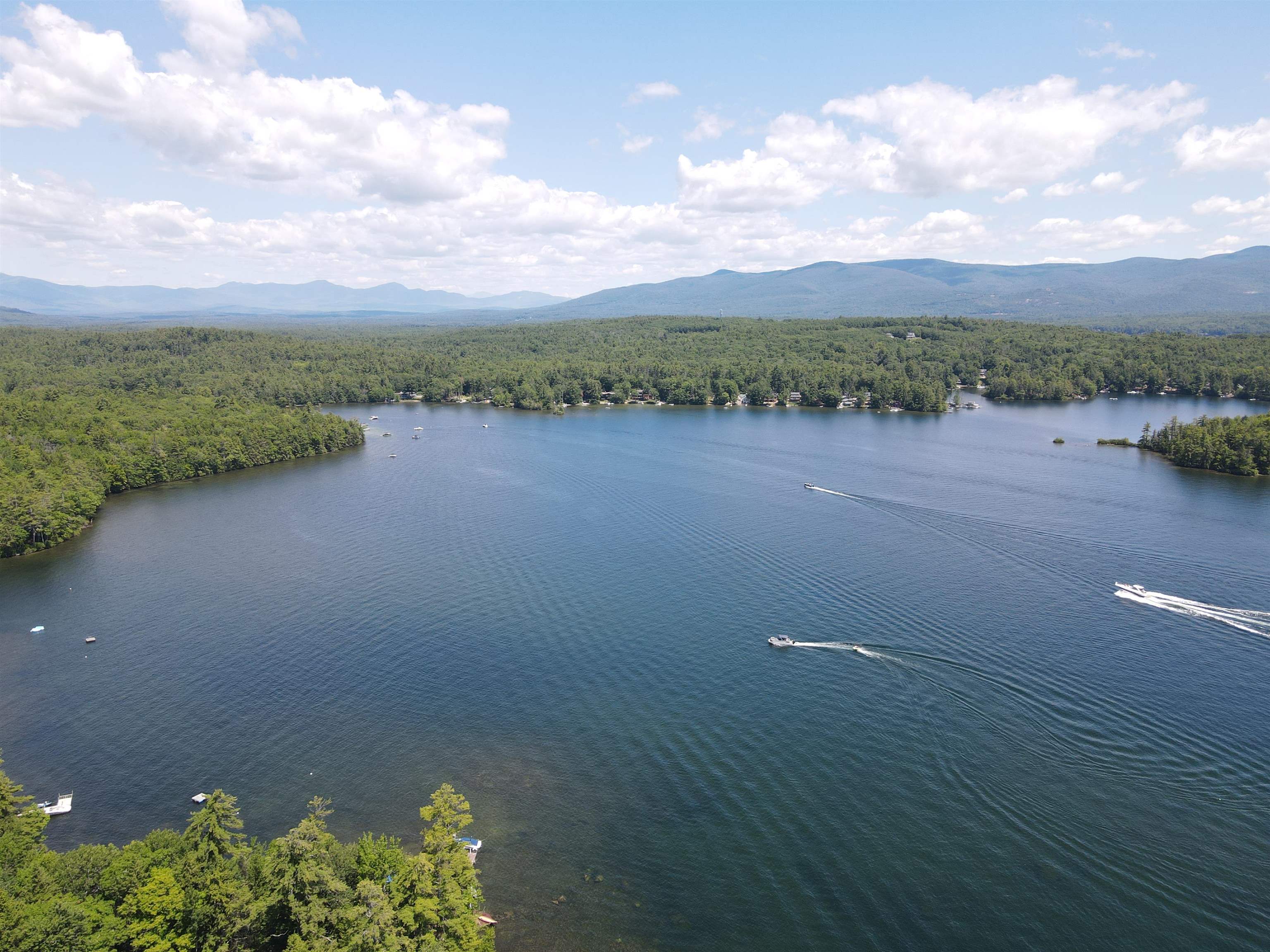 Aerial lake view with boats, wooded shorelines, and distant mountains.