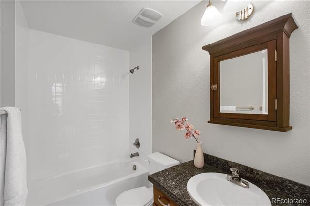 Bathroom with a white bathtub, dark granite vanity, and wood-framed mirrored cabinet.