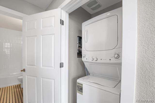 Stacked white washer and dryer in a laundry closet beside an open door.