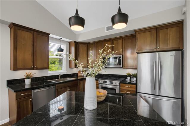 Kitchen with dark wood cabinets, black granite island, stainless steel appliances, and pendant lights.