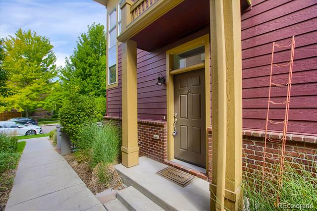 Home entrance with burgundy siding, yellow trim, a brown door, and landscaped walkway.