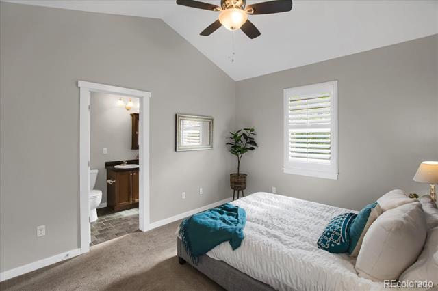 Bedroom with vaulted ceiling, ceiling fan, teal bed accents, and an open doorway to the bathroom.