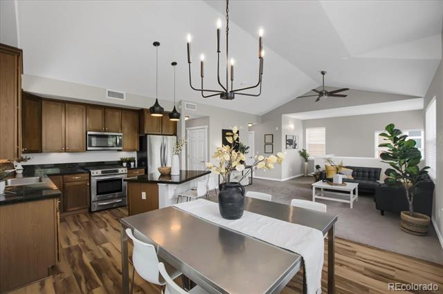 Open-plan kitchen and living room with dark wood cabinets, stainless steel appliances, and vaulted ceilings.