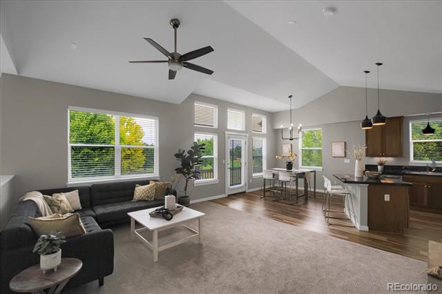 Open-concept living room and kitchen with vaulted ceilings, large windows, and a dark sectional sofa.
