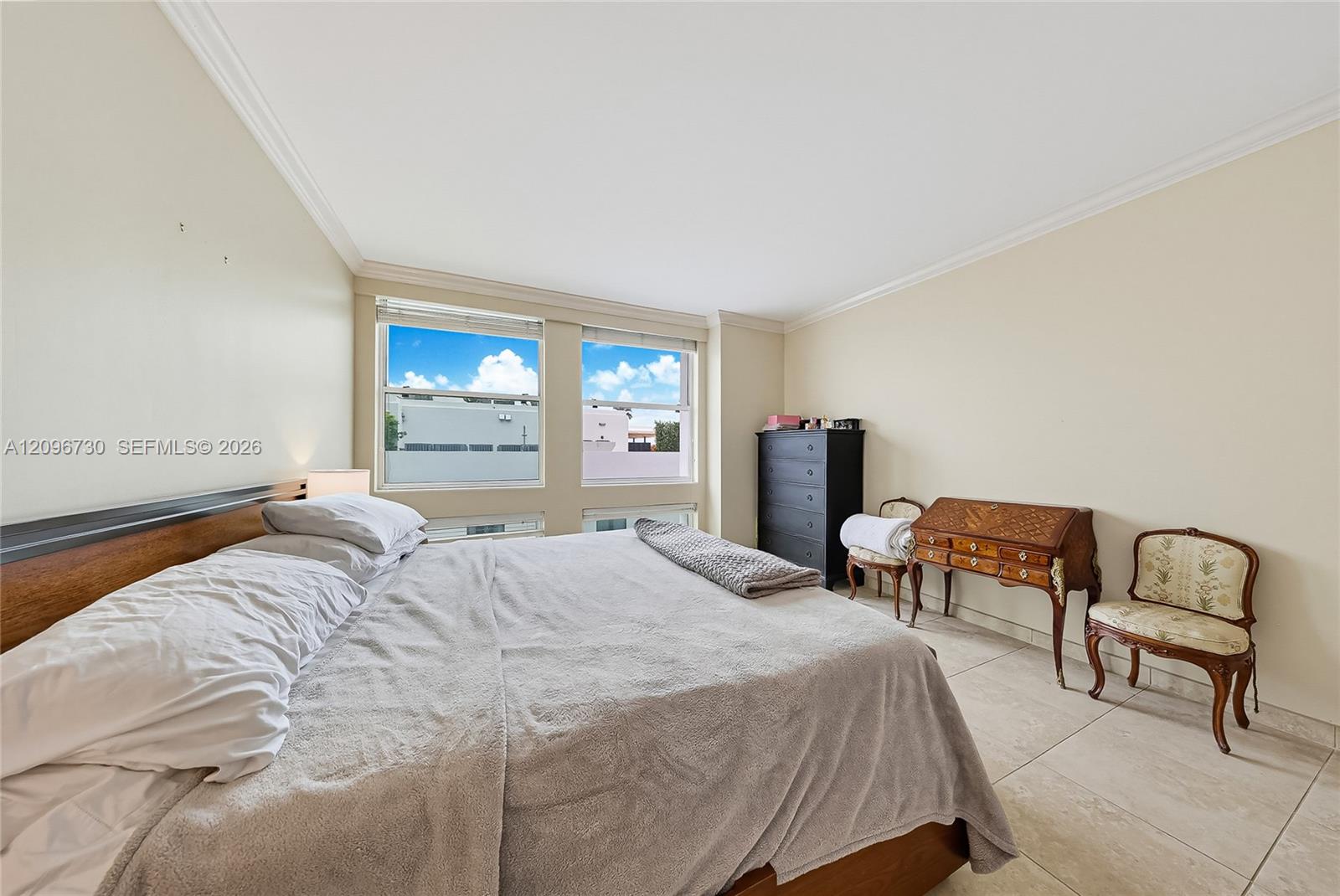 Bedroom with a large bed, two windows, and antique chairs beside a writing desk.