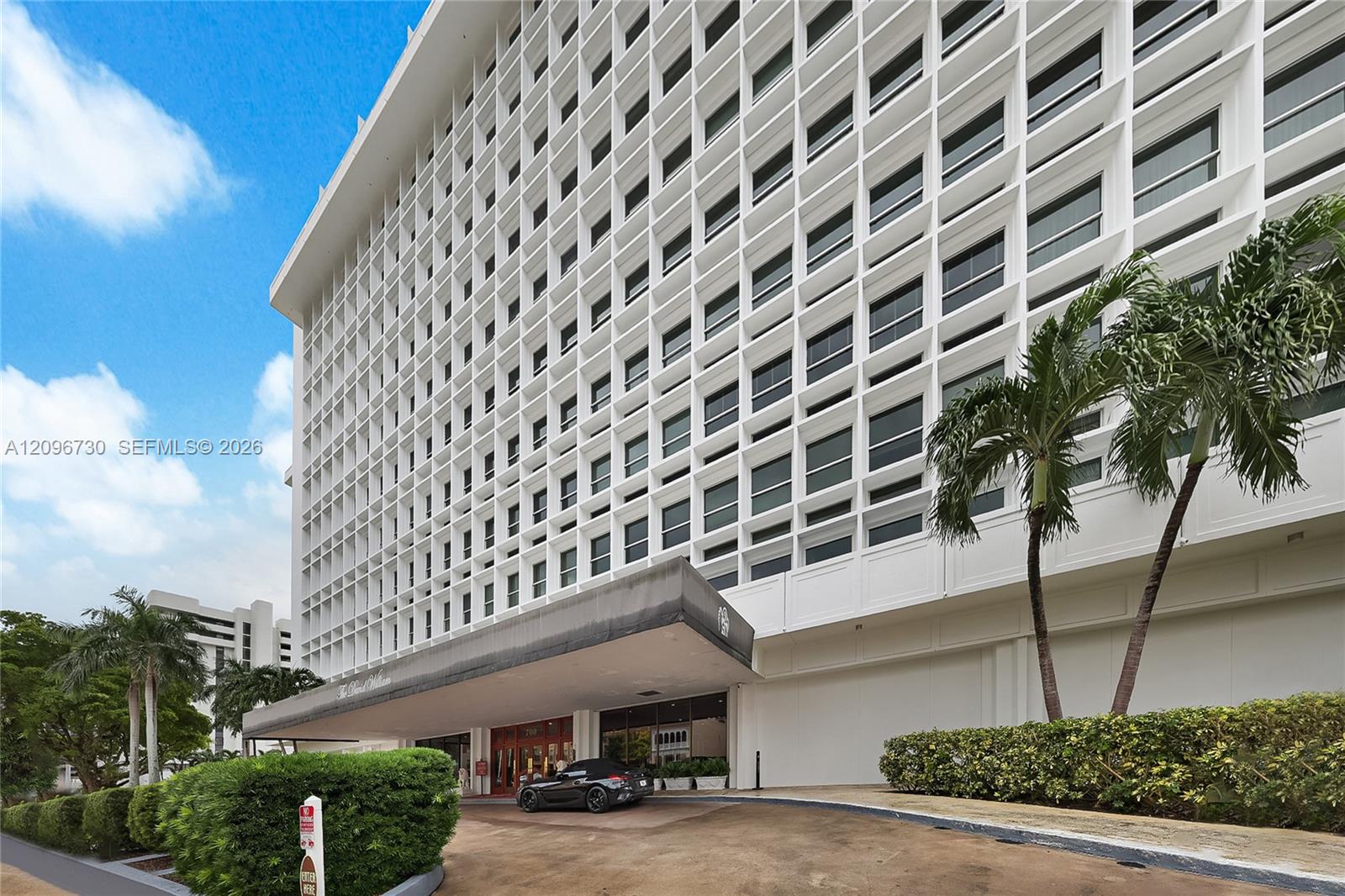 White multi-story residential building with a grid of windows, palm trees, and a covered entrance marked 700.