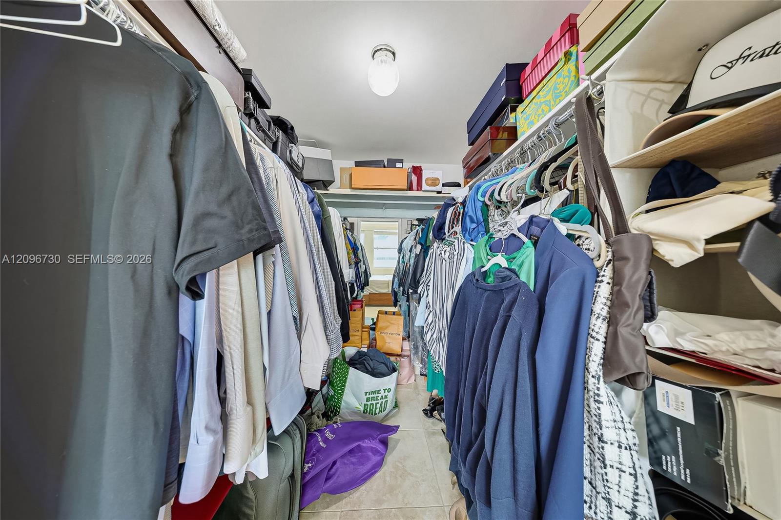 Walk-in closet lined with hanging clothes, overhead shelves, and shopping bags on the floor.