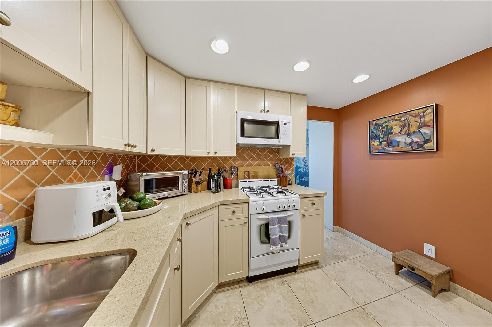Kitchen with cream cabinets, terracotta tile backsplash, granite counters, and a white gas range.
