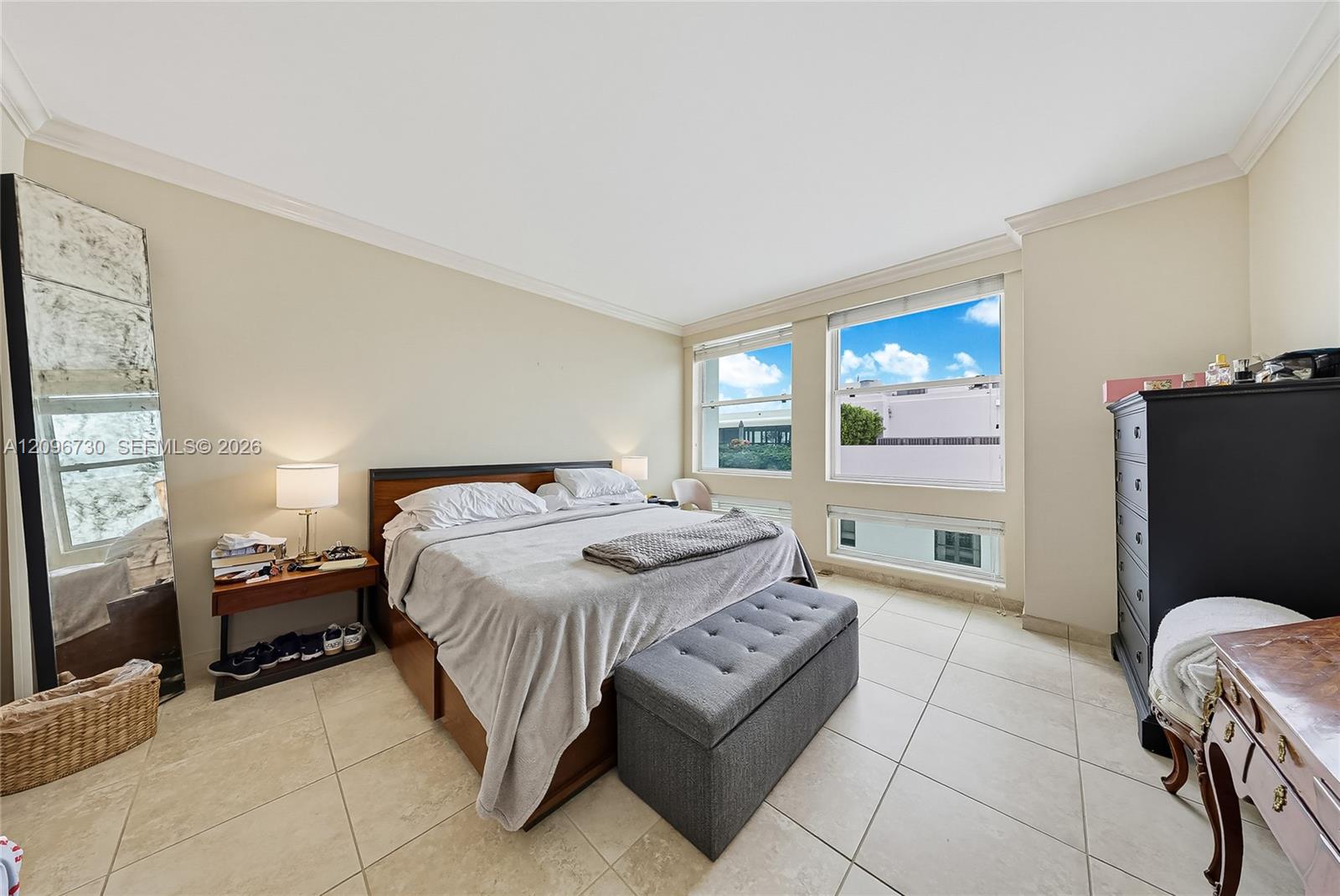 Bedroom with a king bed and gray bench beside large windows.