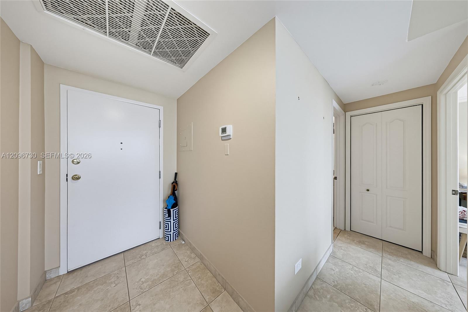 Condominium entry foyer with tiled floors, a white front door, and hallway closet doors.