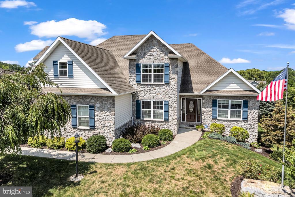 Two-story stone-front home with blue shutters, landscaped yard, and an American flag.