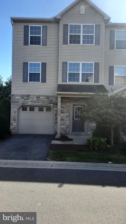 Three-story townhouse with gray siding, stone lower facade, single-car garage, and front driveway.