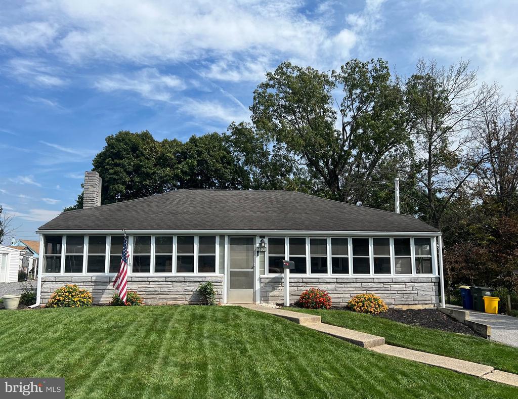 Single-story ranch house with a stone facade, enclosed porch, and landscaped front lawn.