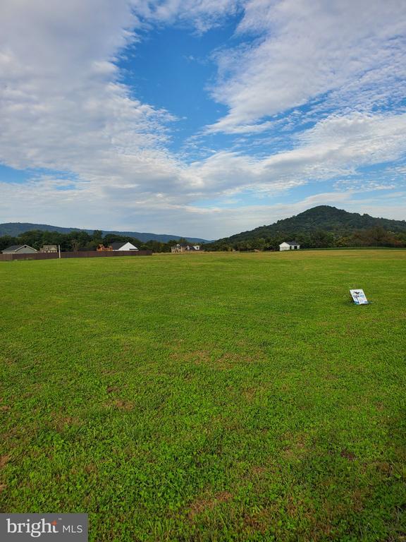 Vacant grassy land with a small real estate sign and wooded hills in the distance.