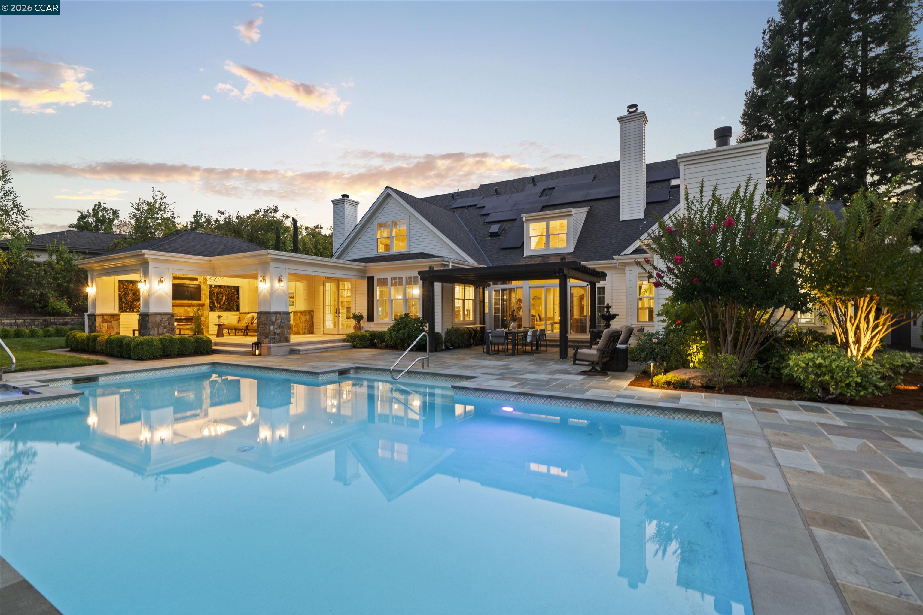 Home’s rear exterior at dusk, with a lit pool, covered patio, and rooftop solar panels.