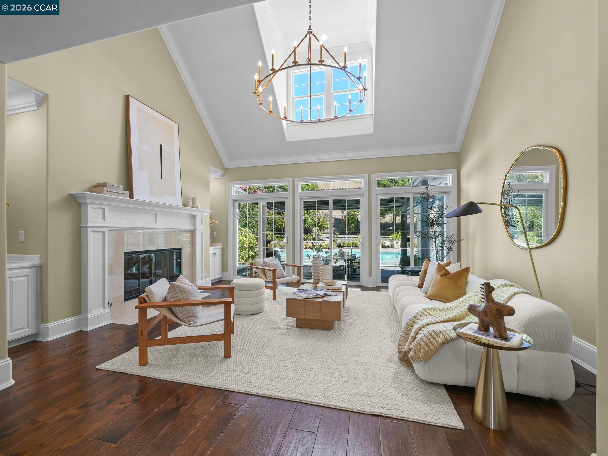 Staged living room with a vaulted skylight, white fireplace, and glass doors overlooking a pool.