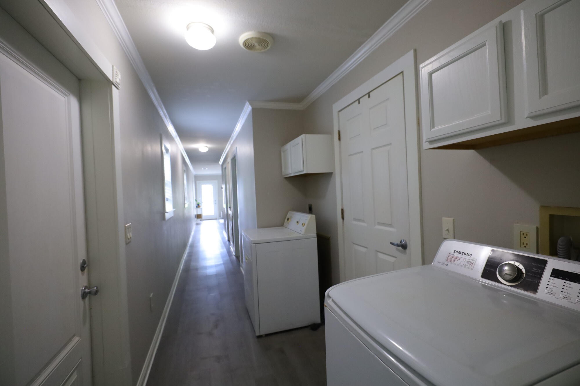Laundry area with two washers, white cabinets, and a long hallway.