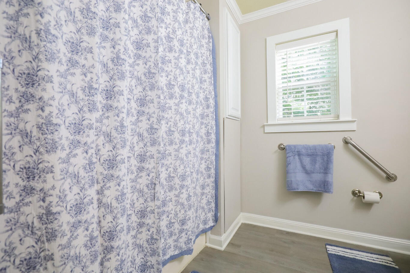 Bathroom with a floral shower curtain, window, blue towel, and metal grab bars.