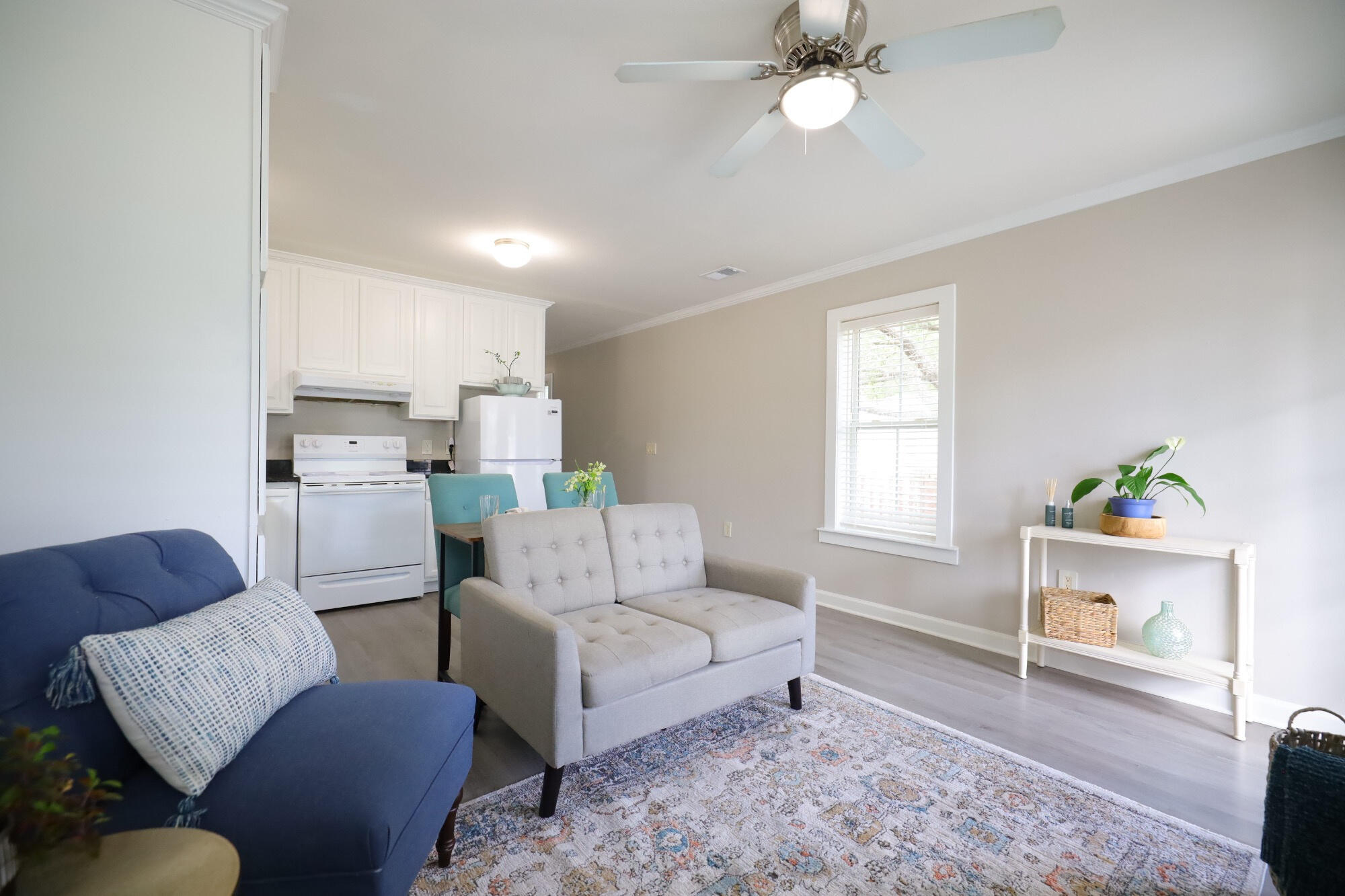 Furnished living room with blue sofa, gray loveseat, patterned rug, and open kitchen.