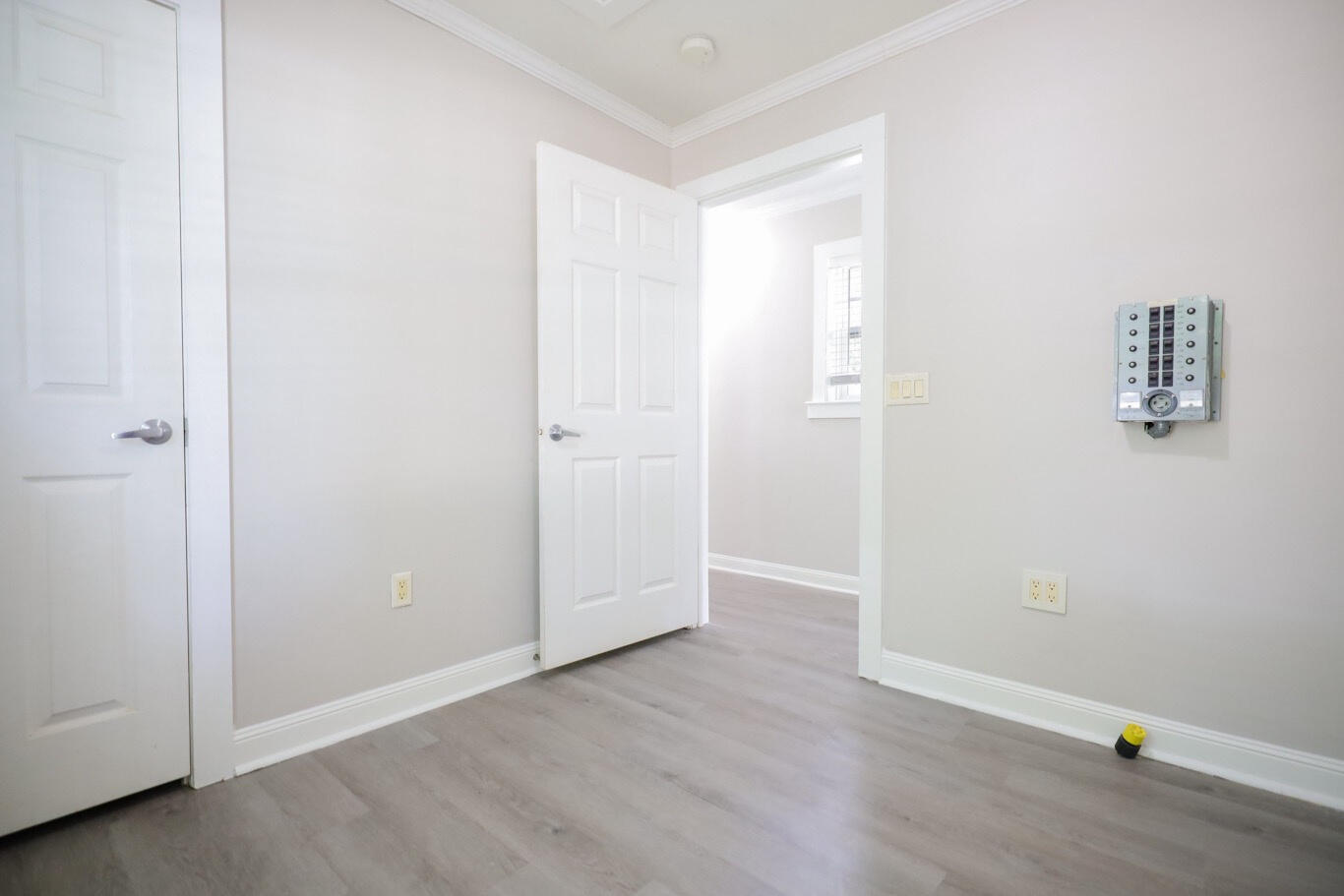 Empty room with pale wood-look flooring, an open doorway, and an electrical panel on the wall.