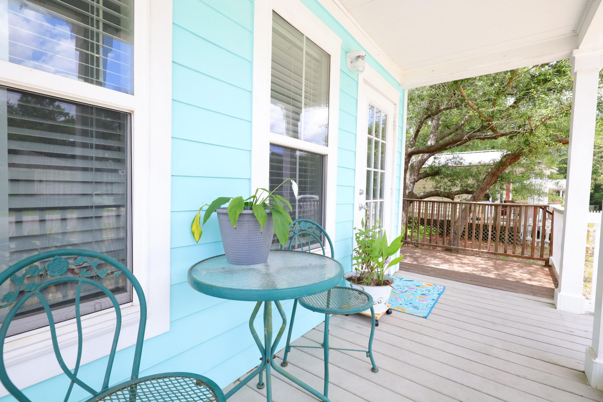 Covered porch with turquoise siding, teal patio furniture, and a wooden deck beneath a large tree.