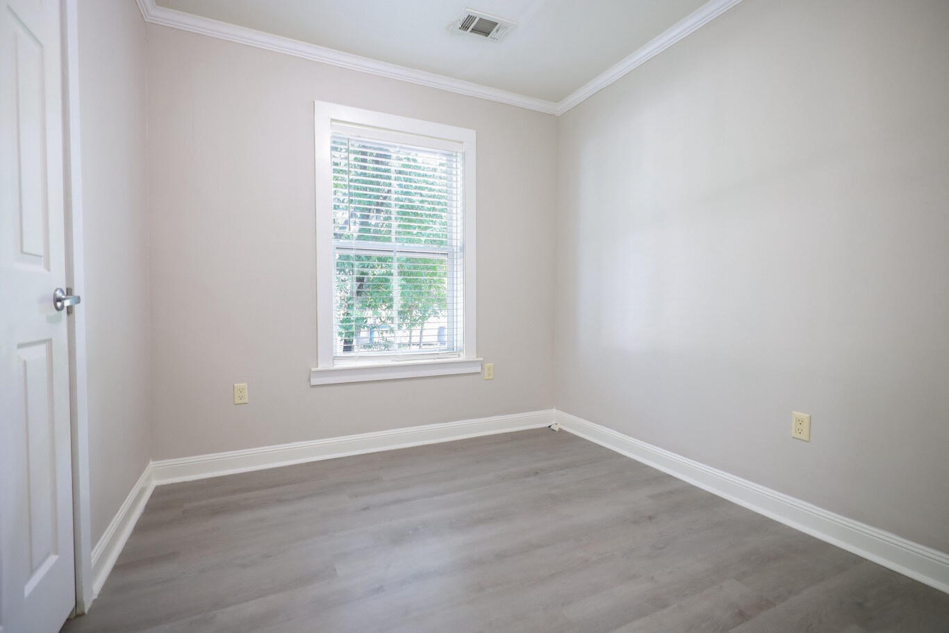 Vacant room with gray plank flooring, white trim, and a window with blinds.