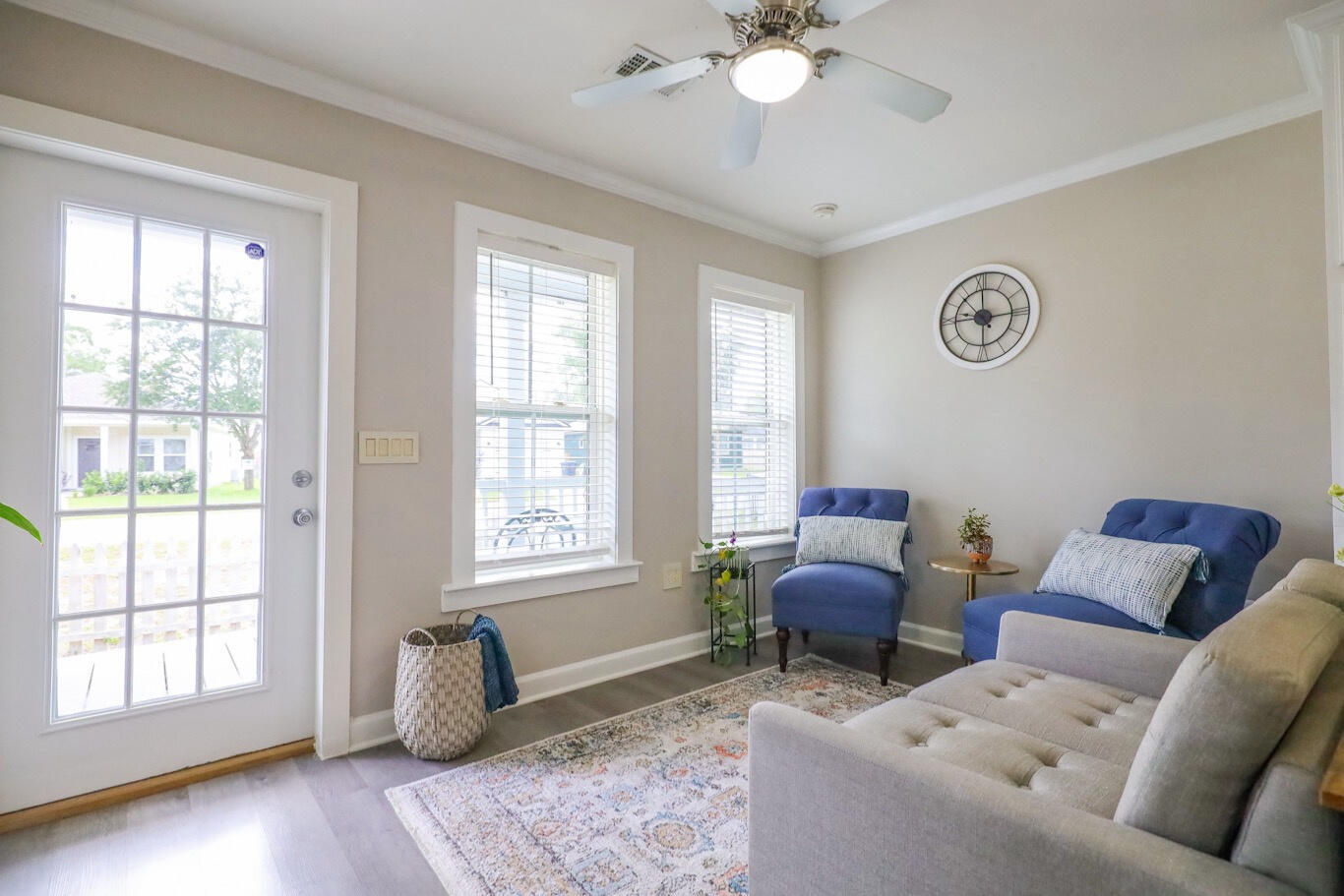 Living room with blue chairs, a light gray sofa, and a glass-paneled door beside bright windows.