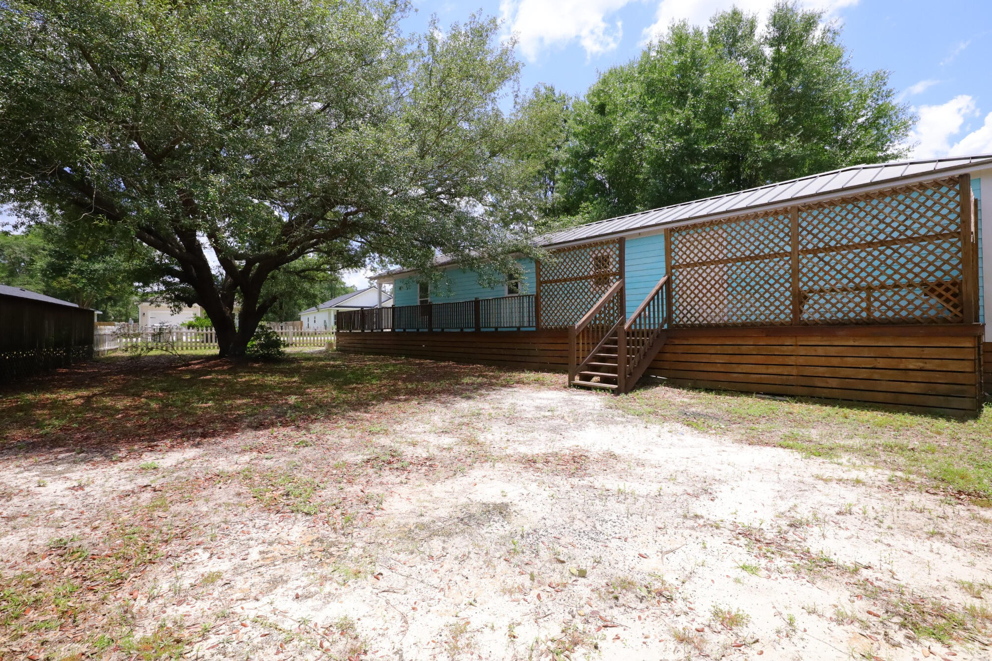 Turquoise home with a raised lattice-sided deck beside a large shade tree and sandy yard.
