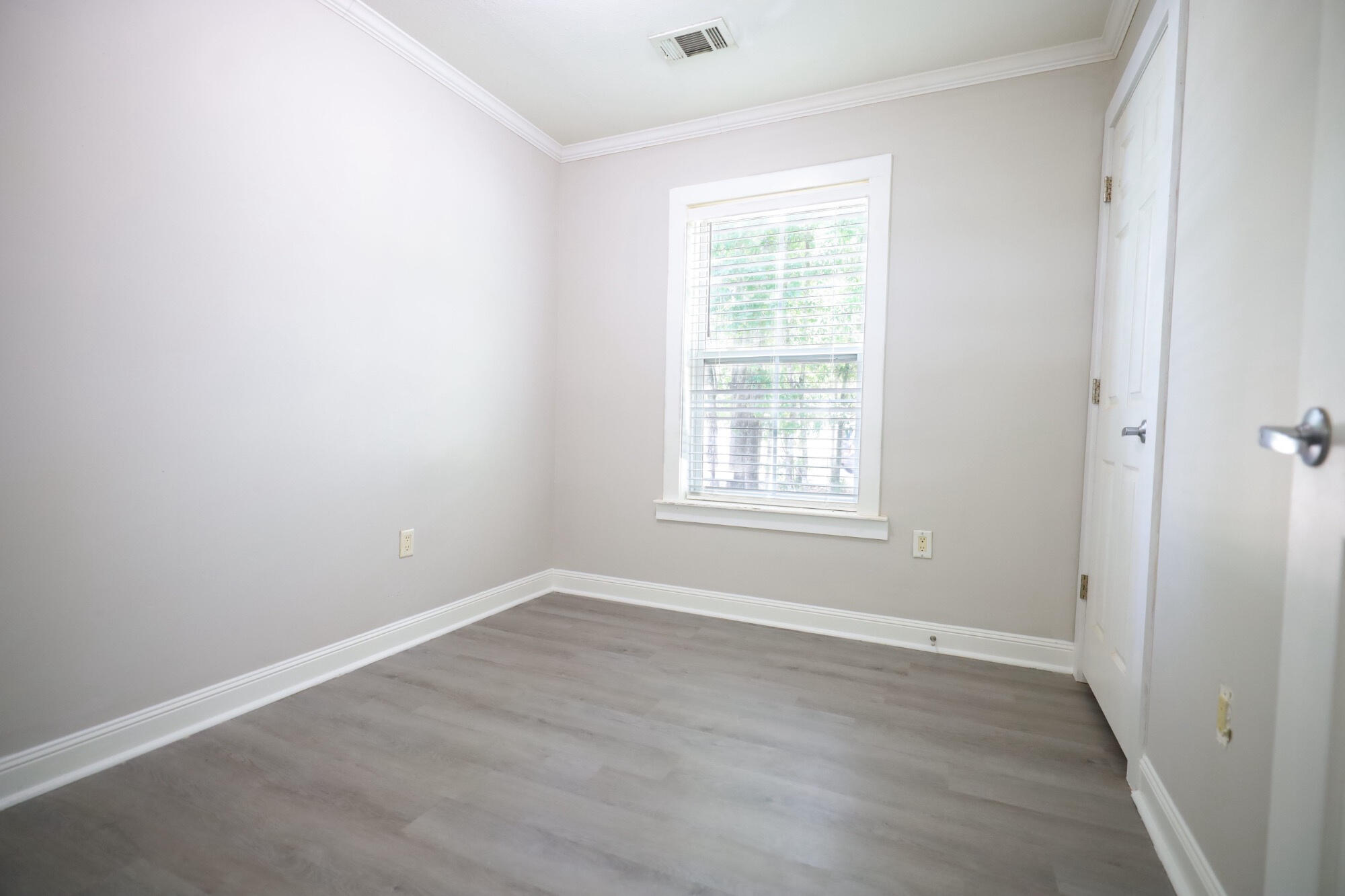 Empty room with gray plank flooring and a window with blinds.