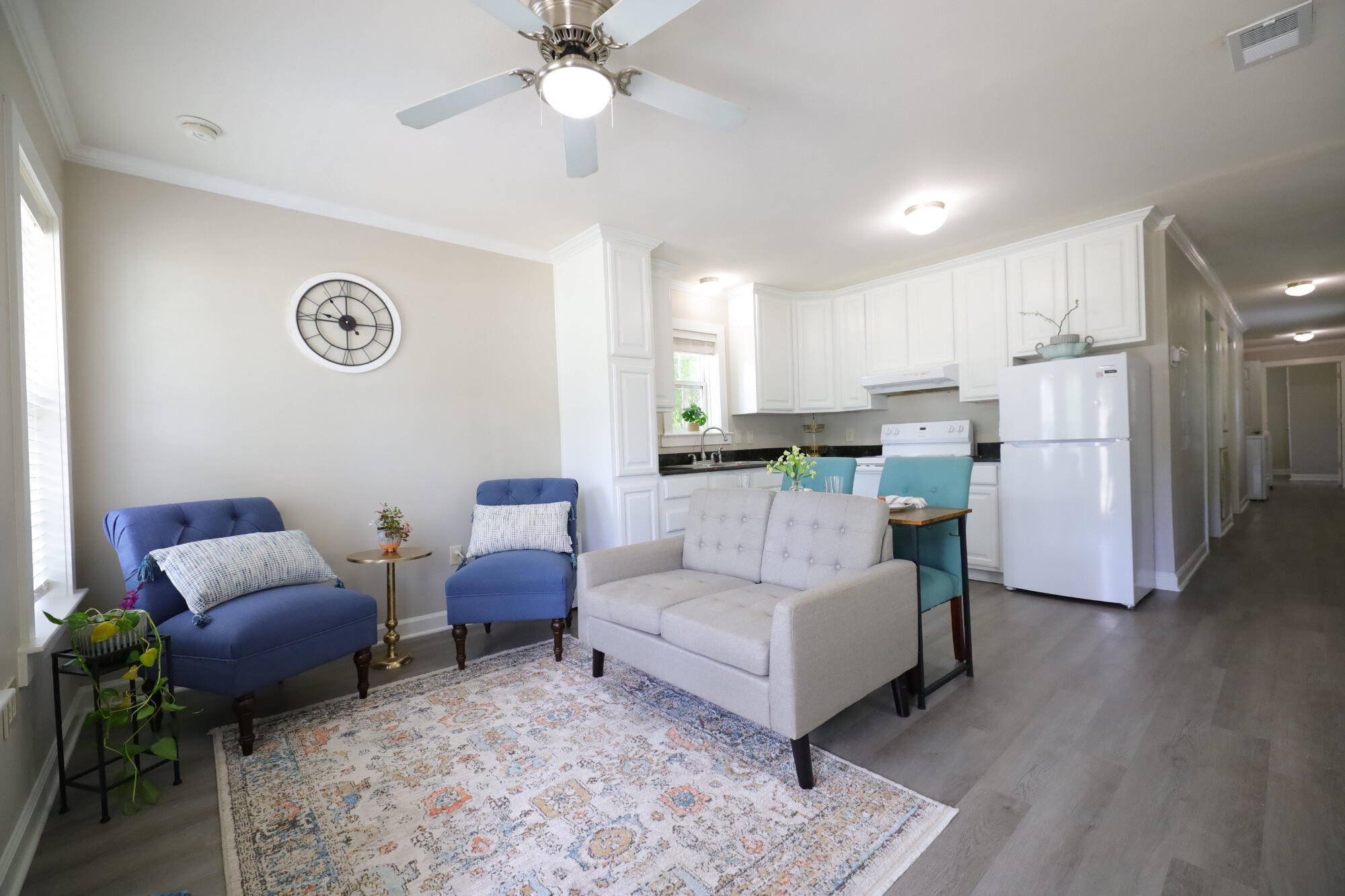 Open-plan living room and kitchen with white cabinetry, gray sofa, blue chairs, and a patterned rug.