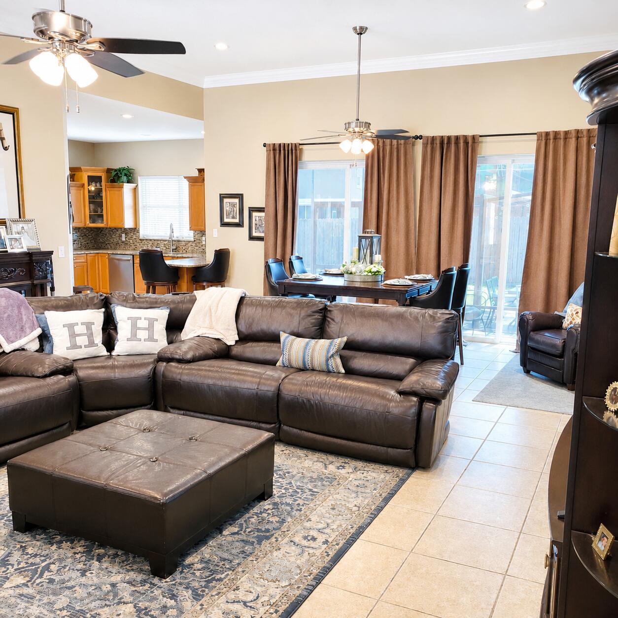 Open-plan living room with a dark leather sectional, dining table, and kitchen beyond.