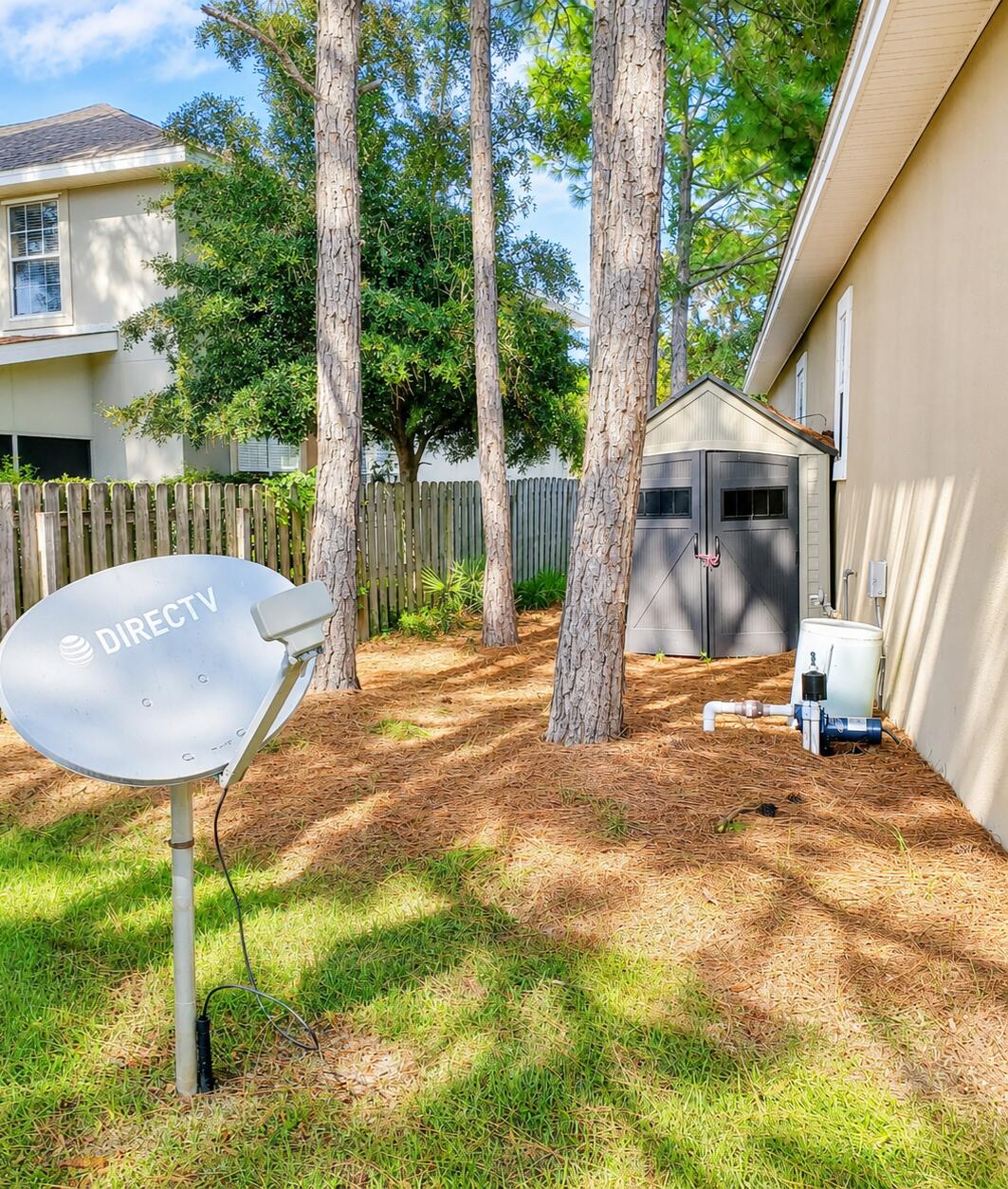 Home side yard with tall trees, a gray storage shed, and a satellite dish.