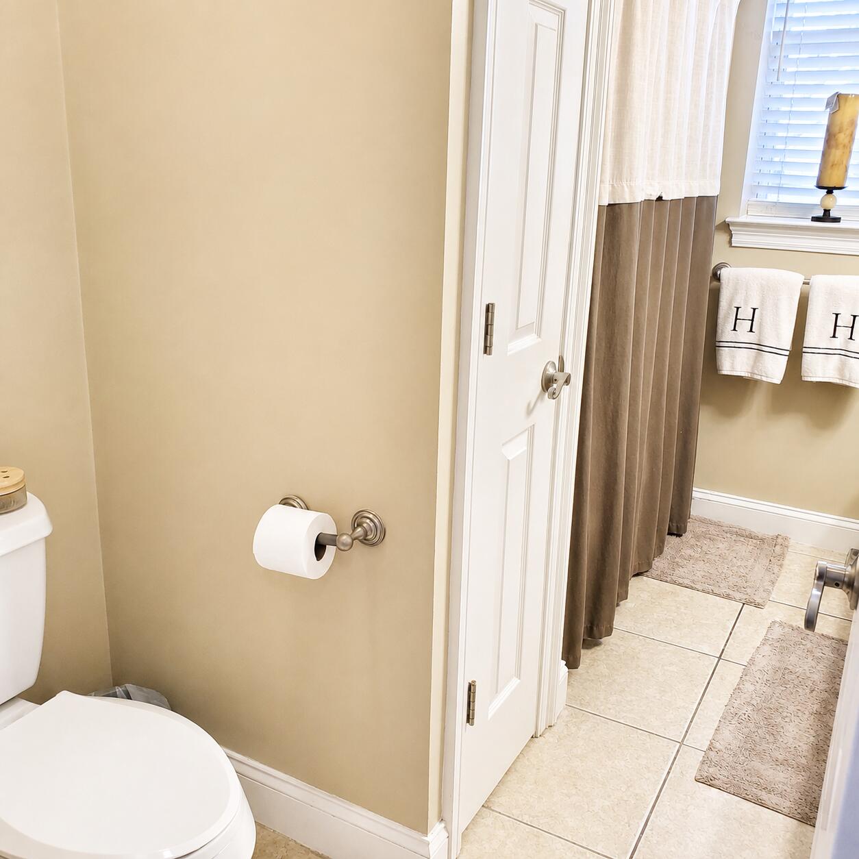 Bathroom with an open door, tiled floor, brown shower curtain, and monogrammed towels.