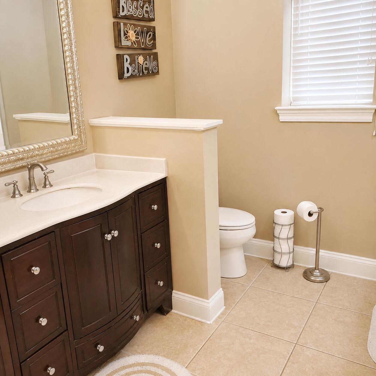 Bathroom with a dark wood vanity, ornate mirror, and toilet behind a half wall.